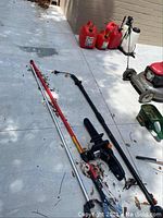 Three red plastic gas cans (two 5 gallons, one 2 gallons), white backpack sprayer, electric chainsaw, and multiple pruners laid out on concrete surface