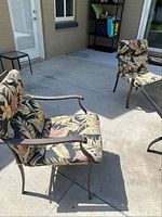 Two metal patio chairs with floral cushions, showing armrests and part of the patio area.