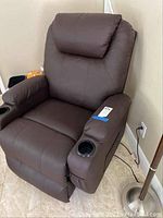 Full view of brown leather massage recliner chair against wall, showing padded headrest and armrests with cup holders.