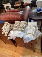 Five white plaster decorative corbel sconce pieces displayed on wooden furniture with bubble wrap under some items.