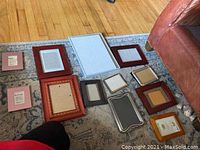 Photo showing 12 assorted picture frames of various sizes and colors laid on carpet.