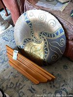 Photo showing decorative round signed wall art plate with gold, blue, brown, and cream swirled abstract design leaning against a couch, with a wooden shelf placed in front of it.