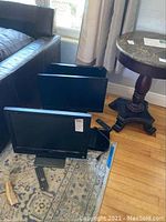 Three screens including the Vizio TV, two computer monitors and a Samsung Blu-ray player placed on floor near couch.