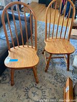 Two oak high back chairs placed on a rug with a leather couch nearby. Shows overall structure and style of chairs.