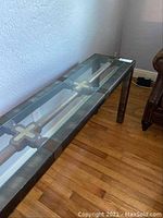Full length view of metal and glass sofa table against wall on wood floor.