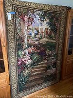 Full view of the large hanging tapestry showing the garden stairs, cottage, flowers, and urn scene inside an ornate border.