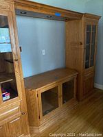 Front view of oak entertainment center showing lower and tall side cabinets with glass beveled doors.