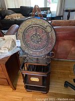 Front view of the mosaic decorative plate on metal stand atop the wooden magazine rack.