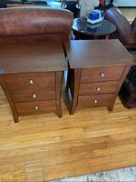 Two medium brown wooden end tables with three drawers each, placed on hardwood floor next to leather seating.