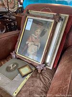 Group shot of framed vintage art and photographs displayed on a chair, includes the 12x16 art print with ornate corner frame and smaller photos.
