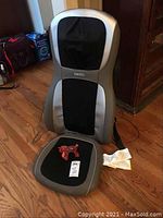 Photo of Homedics massage chair showing front view with label and handheld massager placed on seat cushion