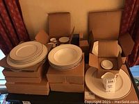 Photo showing stacks of Mikasa plates including salad, soup, dinner plates, and boxed items with cups and saucers plus Waterford crystal vase.