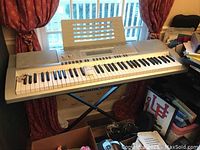 Full view of Casio WK-210 electronic keyboard on X-style stand showing keyboard length and surroundings.