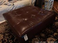 Top and side view of a brown leather ottoman showing tufted button detail and surface wear.