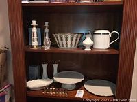 Shelf displaying Lenox and Gorham porcelain and glass tableware including cake plates, candy dish, serving plates, candlestick holders, salt and pepper shakers.