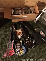 Four Guitar Hero guitar controllers laid on carpet, next to open boxes with games.