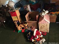 Photo showing wicker dollhouse toy box, wooden cabinet with cloth bins, assorted toys and costume items on carpeted floor.