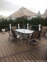 Full view of the outdoor patio table with glass top, six matching chairs, and Wilson umbrella on deck.