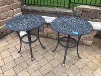 Two matching side tables side by side showing full view of tops and bases on patio pavers