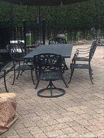 Overall view of black metal patio table and six chairs under umbrella