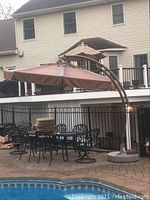 Poolside patio showing full view of brown cantilever umbrella next to metal patio furniture.