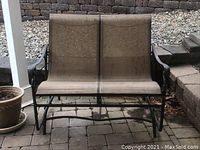 Front view of double swing chair showing metal frame, two fabric seats, and signs of weathering.