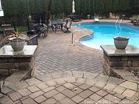 Two filled outdoor planter pots flanking pool entrance, positioned on short stone pillars at the poolside patio area.