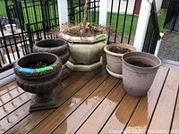 Photo showing all five planters on outdoor deck, varied styles and sizes with soil and dried plants inside.