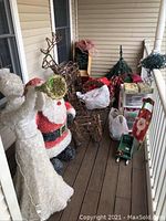 Wide view of front porch showing artificial Christmas tree, Santa figure, angel figure, reindeer and sleigh yard decorations, storage shelves with holiday supplies, and pre-lit wreath boxes stacked.