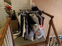 Clothing rack holding assorted garments in a hallway corner, with plastic bags of clothes beneath