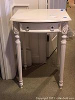 Straight front view showing white side table with curved front drawer and decorative carved legs.