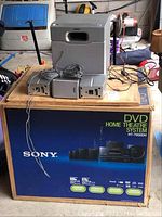 Sony HT-7000DH Home Theater system main components on top of original blue Sony box. Visible are main DVD/amplifier unit, subwoofer, satellite speakers, and cables.