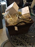 Woven dark brown basket with handle containing gold-colored samovar set, glass dishes, and two white boxed mug sets.