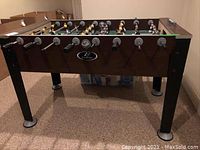 Front side view of dark wood finished foosball table with player rods and circular base caps on legs