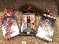 Photo of three sealed Barbie collectible dolls in original packaging lying on carpet, each decorated with red ribbon bows.