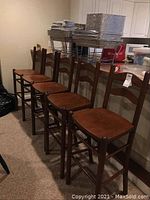 Five wooden barstools lined up against a countertop/bar area. Shows the full set and arrangement.