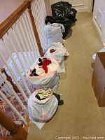 Five large bags filled with assorted clothing placed on a carpeted stair landing.