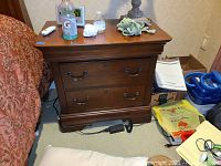 Front view of one of the dark brown wood nightstands with two drawers, showing metal handles and some items placed on top.