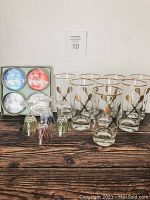 Full lot including wooden accordion wine rack, eight gold rimmed highball glasses with dart design, four crystal Harlequin sherry glasses, and a boxed set of four Hawaii souvenir coasters in blue, red, black, and white