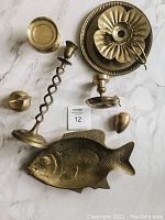 Top view of all seven brass items laid out including the fish tray, flower candle holder, finger loop candle holder, egg paperweight, hammered plate, barley twist candle holder, and apple bell.