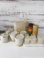 Full view of vintage Tupperware items showing cereal keeper, cream and sugar set, condiment caddy, cups, and other items.