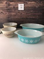 Four vintage Pyrex bowls: two turquoise Snowflake Blue casserole dishes and two beige Forest Fancies patterned bowls.
