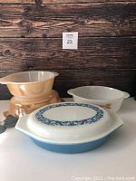 Four vintage casserole dishes: two peach FireKing pieces without lids, two Pyrex divided dishes with one lid showing blue floral decoration.