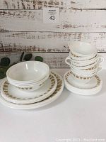 Set of 8 bowls, 8 side plates, 8 cups, and 8 saucers stacked with visible gold floral pattern on white dishes.