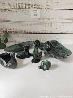 All Blue Mountain Pottery items shown together including two leaf-shaped dishes and five ceramic animal figurines on a white surface in front of a rustic wood background.