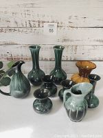 Nine Blue Mountain Pottery vases in green and brown drip glaze, assorted shapes and sizes.