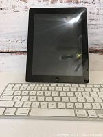 Front view of iPad 2 with black screen bezel next to wireless white keyboard with dock stand.