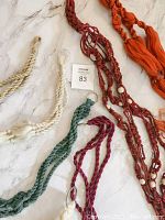 Top angle view of multiple macrame plant hangers in assorted colors and styles laid out on white marble surface.