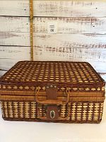 Closed rectangular wicker picnic basket with leather handle and metal latch on front, placed against light wood background with measuring stick showing size.