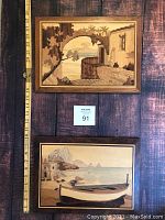 Framed etched wood pictures showing coastal themes with boats and buildings in natural wood tones, placed on wooden floor with measuring stick